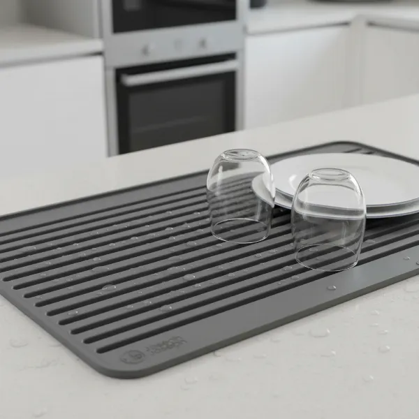 A grey Joseph Joseph Flume Folding Mat laid out on a clean kitchen counter with a few dishes drying on it.