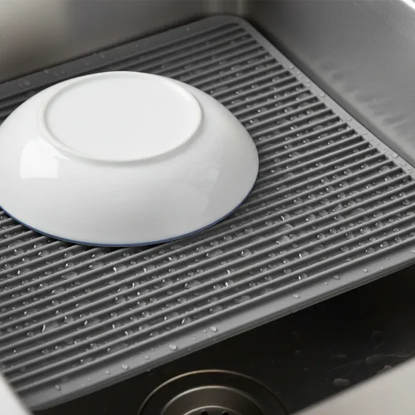 A close-up shot of the OXO Silicone Sink Mat in a kitchen sink, highlighting its ribbed design and grey color, with a dish resting on it