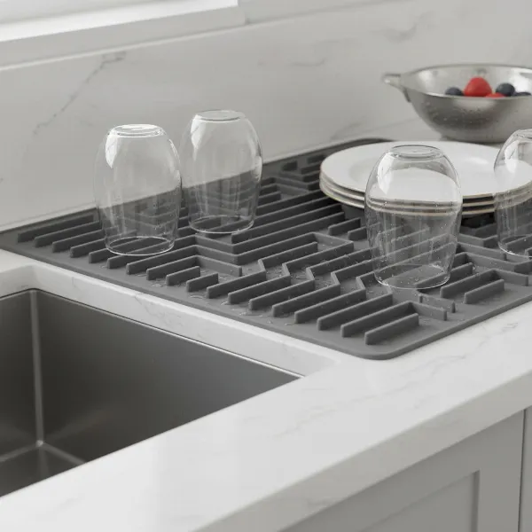 A grey silicone dish drying mat with raised ridges on a clean kitchen counter, next to a sink.